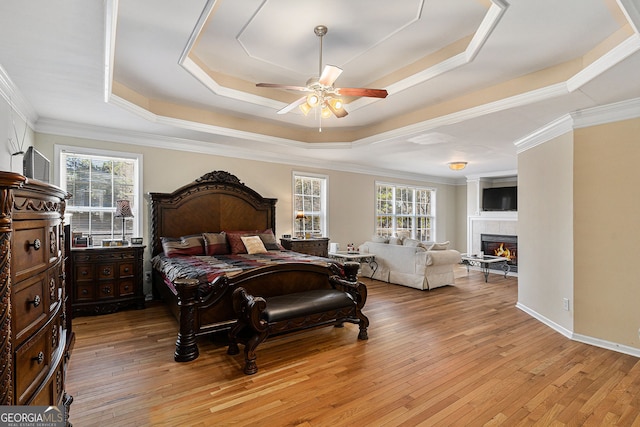 bedroom with a raised ceiling, a tile fireplace, and light wood-style flooring