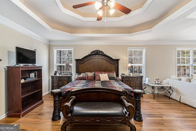 bedroom with crown molding, baseboards, a raised ceiling, and light wood-style floors