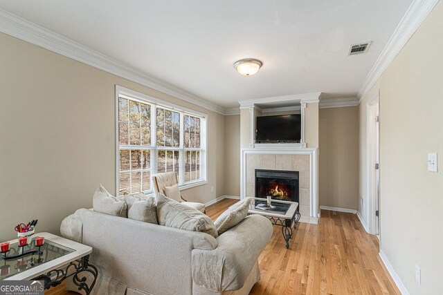 living area featuring crown molding, visible vents, light wood-type flooring, and a tiled fireplace