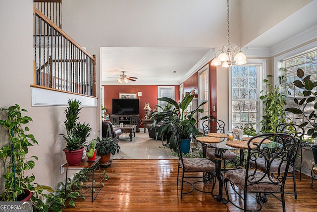dining space featuring light wood-style flooring, crown molding, ceiling fan with notable chandelier, and a towering ceiling