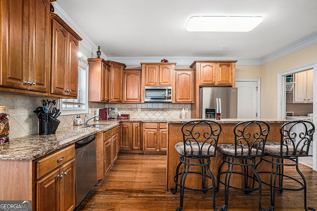 kitchen with ornamental molding, appliances with stainless steel finishes, dark wood-style flooring, a sink, and a breakfast bar area