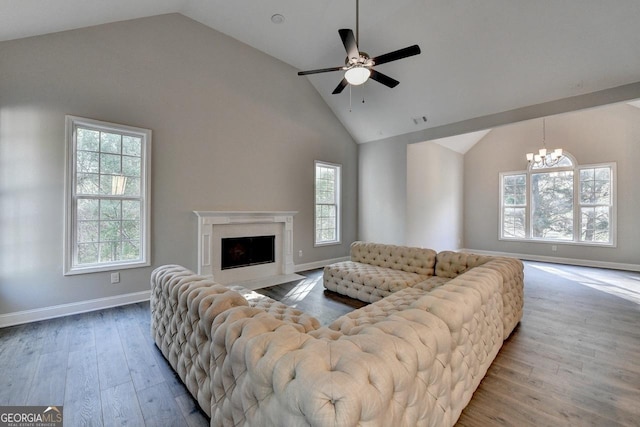 living area featuring a fireplace, visible vents, high vaulted ceiling, ceiling fan with notable chandelier, and wood finished floors