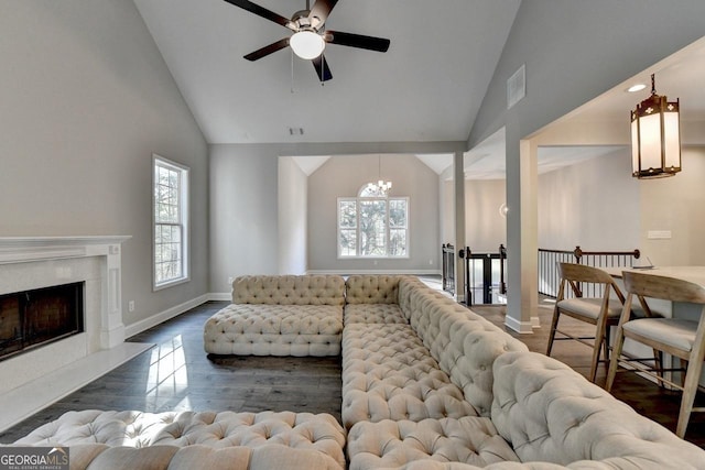 living area with high vaulted ceiling, a wealth of natural light, ceiling fan with notable chandelier, and baseboards