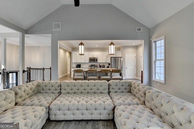 living area with light wood finished floors, high vaulted ceiling, and visible vents