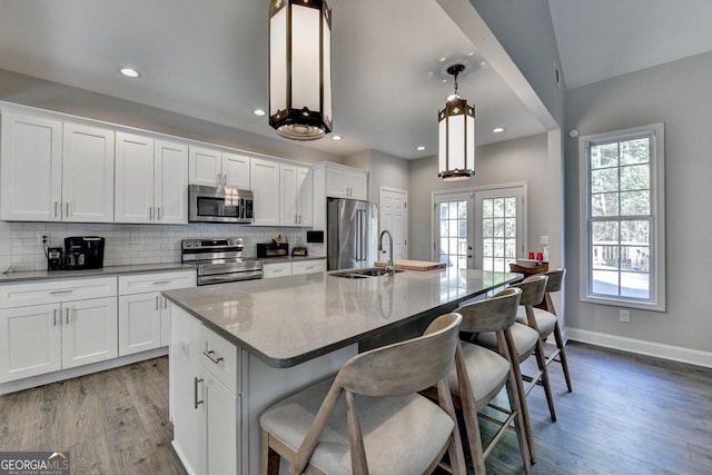 kitchen featuring a sink, stainless steel appliances, a center island with sink, french doors, and light wood finished floors
