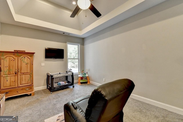 living area featuring carpet floors, ceiling fan, a tray ceiling, and baseboards