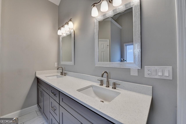 full bath with double vanity, marble finish floor, a sink, and baseboards
