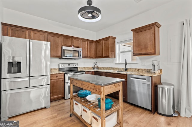 kitchen with light wood-style floors, appliances with stainless steel finishes, a sink, and light stone countertops