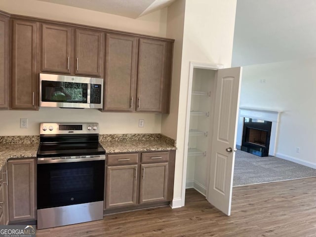 202 Gamel Rd, Dallas, GA 30157 - kitchen with baseboards, a fireplace, wood finished floors, stainless steel appliances, and light stone counters