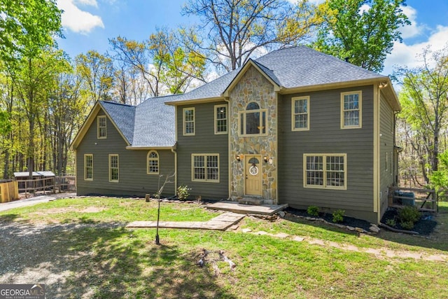 view of front of house featuring a shingled roof, stone siding, and a front lawn