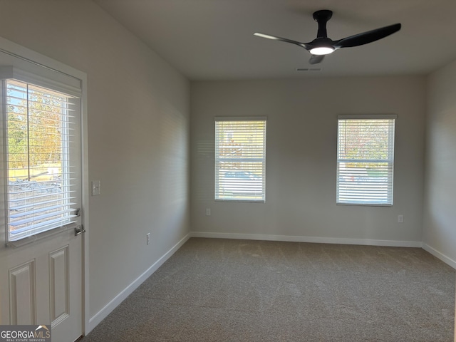 carpeted spare room with visible vents, baseboards, and ceiling fan