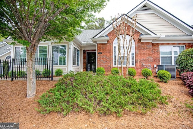 view of front facade with brick siding, fence, and central air condition unit