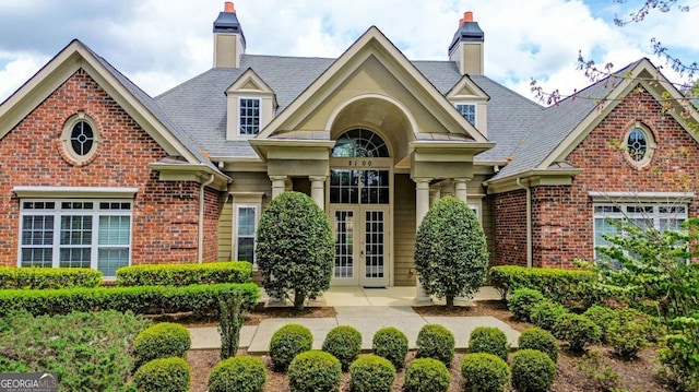 view of front of property with french doors, brick siding, and a chimney