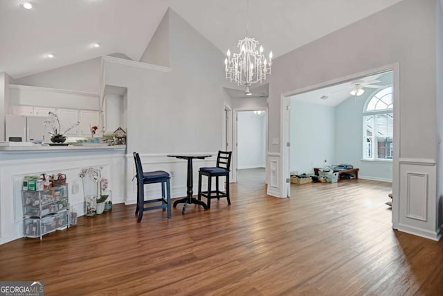 dining space with high vaulted ceiling, ceiling fan with notable chandelier, baseboards, and wood finished floors
