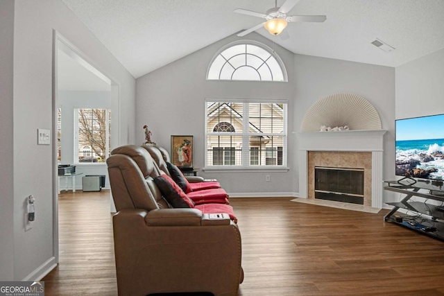 living area with visible vents, a ceiling fan, wood finished floors, a tile fireplace, and lofted ceiling