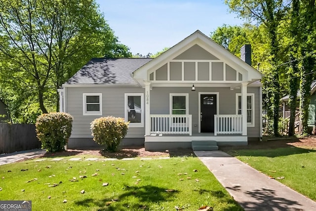 view of front of property featuring a shingled roof, a porch, a chimney, and a front lawn