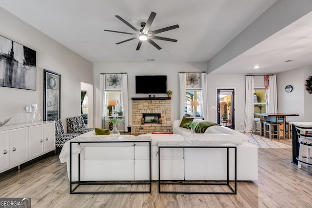living area featuring a fireplace, light wood-style flooring, and ceiling fan