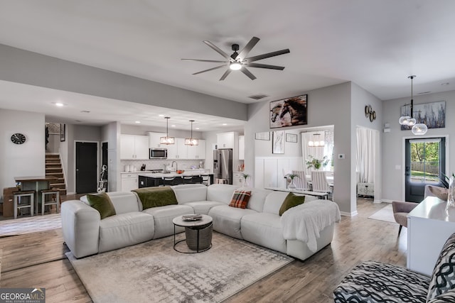 living area featuring stairs, ceiling fan with notable chandelier, light wood-style floors, visible vents, and recessed lighting