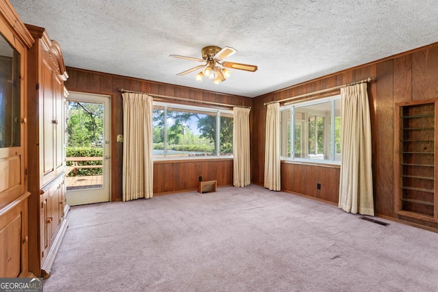 unfurnished room with a healthy amount of sunlight, wood walls, a ceiling fan, and visible vents