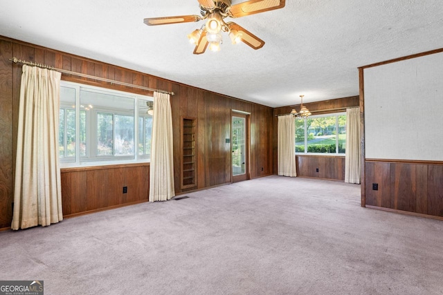 empty room featuring wood walls, visible vents, ceiling fan with notable chandelier, and carpet floors