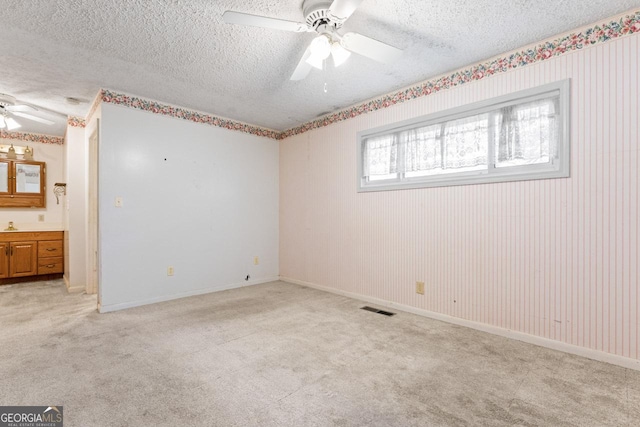 spare room featuring a textured ceiling, ceiling fan, light carpet, and visible vents