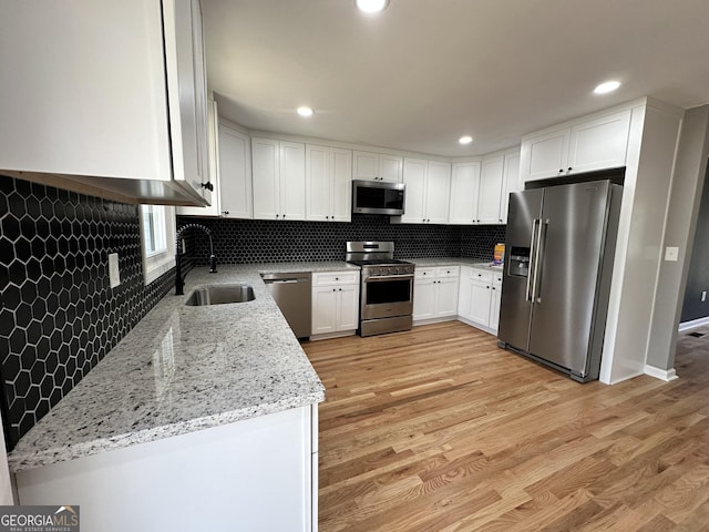 kitchen with white cabinets, light stone counters, a sink, stainless steel appliances, and backsplash