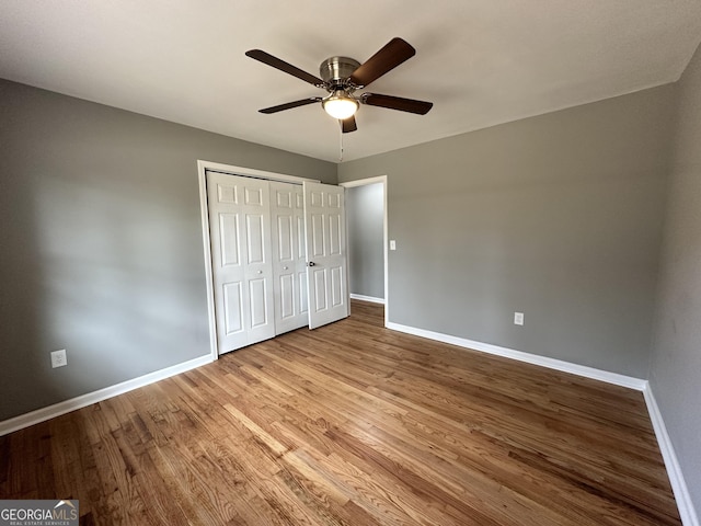 unfurnished bedroom with a ceiling fan, wood finished floors, baseboards, and a closet
