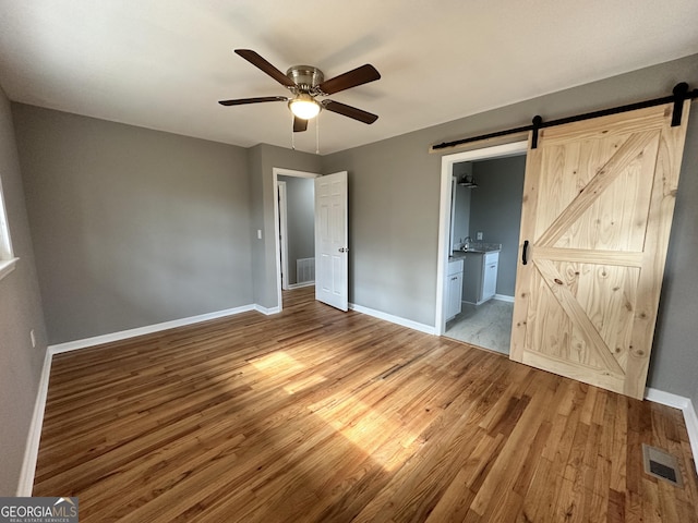 unfurnished bedroom featuring wood finished floors, baseboards, visible vents, and a barn door