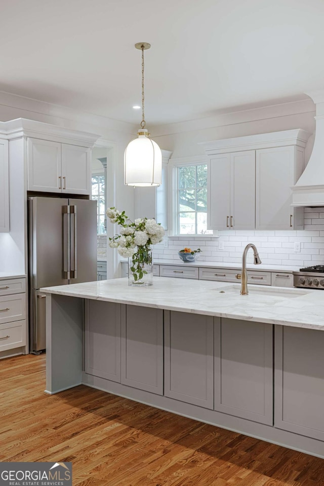 kitchen with white cabinets, light stone countertops, high end fridge, and backsplash
