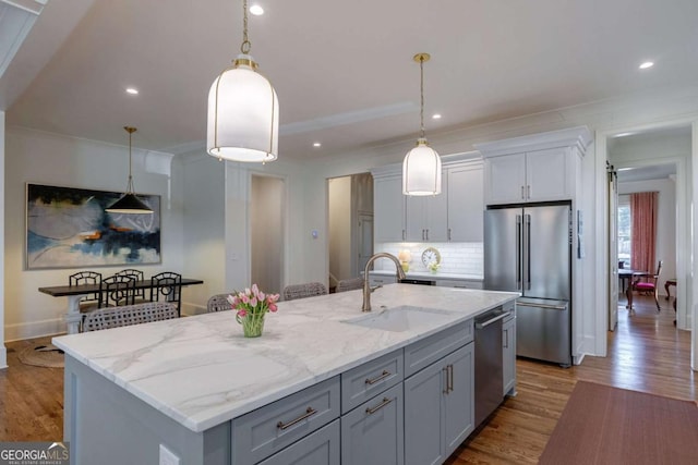 kitchen with a sink, white cabinetry, wood finished floors, light stone countertops, and stainless steel appliances