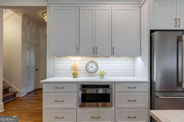 kitchen with wood finished floors, white cabinetry, backsplash, and appliances with stainless steel finishes