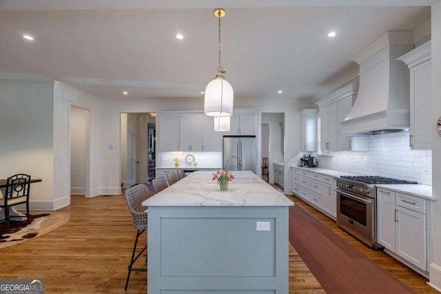 kitchen featuring tasteful backsplash, a breakfast bar, a kitchen island with sink, premium appliances, and custom range hood