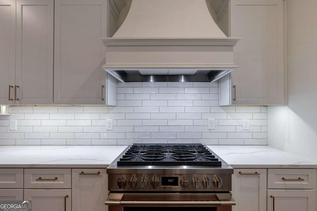 kitchen with tasteful backsplash, premium range hood, high end stove, and light stone countertops