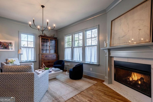 sitting room with a notable chandelier, baseboards, crown molding, a fireplace with flush hearth, and wood finished floors