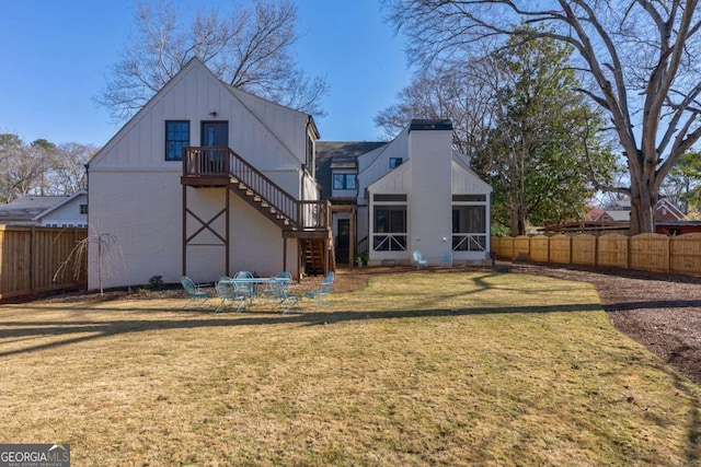 rear view of property with stairway, brick siding, a fenced backyard, a yard, and a sunroom