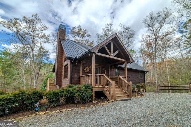 back of house featuring stairway, gravel driveway, a chimney, a wooden deck, and metal roof