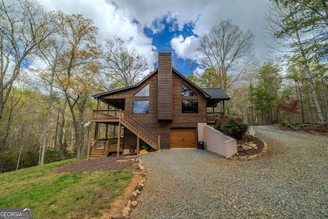 chalet / cabin with a chimney, an attached garage, metal roof, gravel driveway, and stairs