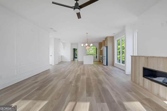 644 Glendale Rd, Scottdale, GA 30079 - unfurnished living room with a fireplace, light wood-style floors, ceiling fan with notable chandelier, and a decorative wall