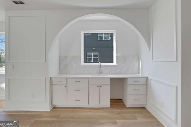 644 Glendale Rd, Scottdale, GA 30079 - interior space featuring light wood-style flooring, visible vents, decorative backsplash, arched walkways, and a sink
