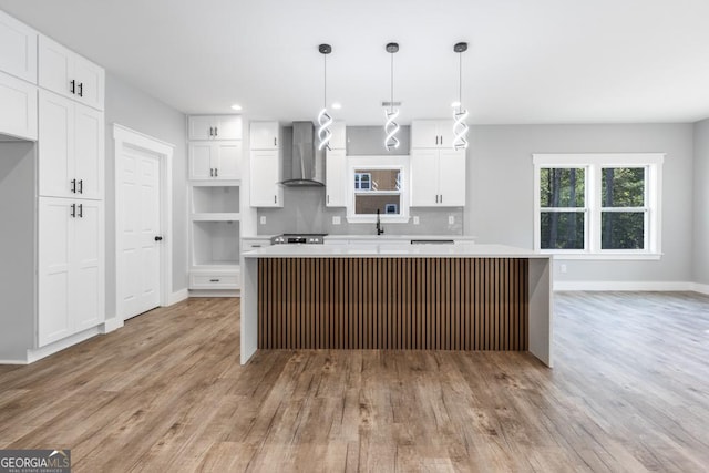kitchen with light wood-style floors, wall chimney exhaust hood, a kitchen island, baseboards, and backsplash