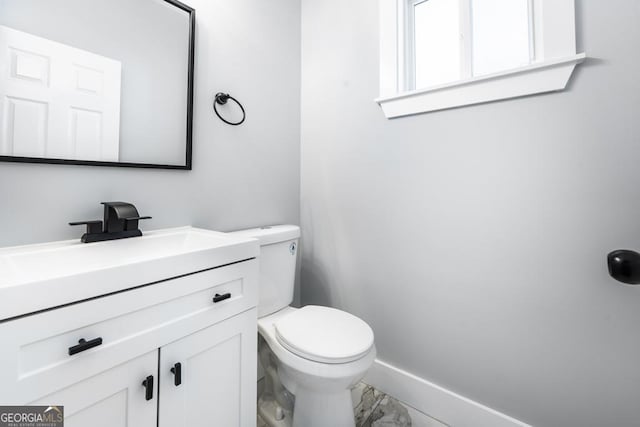 half bath featuring vanity, marble finish floor, and toilet