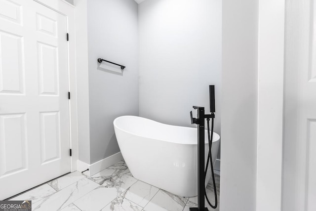 bathroom with a freestanding tub, marble finish floor, and baseboards