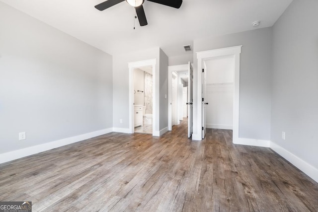 unfurnished bedroom with a closet, baseboards, a walk in closet, visible vents, and wood finished floors