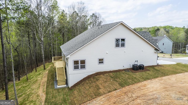 view of side of property featuring a yard, stairway, a shingled roof, and central air condition unit