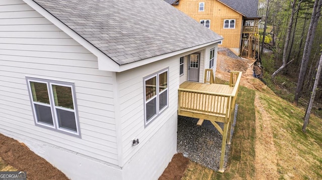 view of side of home with a lawn, a deck, and a shingled roof