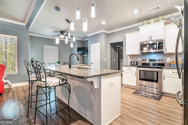 kitchen with crown molding, a sink, light wood-style floors, appliances with stainless steel finishes, and visible vents