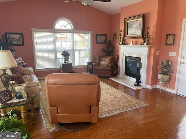 living area with ceiling fan, a fireplace, vaulted ceiling, wood finished floors, and baseboards