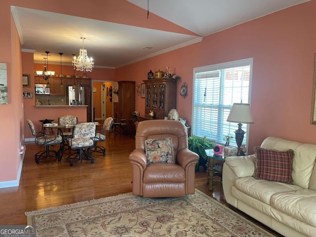 living area with a notable chandelier, baseboards, vaulted ceiling, ornamental molding, and wood finished floors