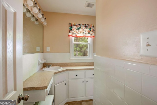 bathroom with vanity, wainscoting, visible vents, and tile walls