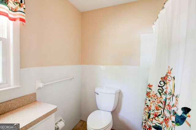 bathroom featuring vanity, curtained shower, a wainscoted wall, toilet, and tile walls